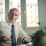 Home A mature man in professional attire smiling in an office setting.